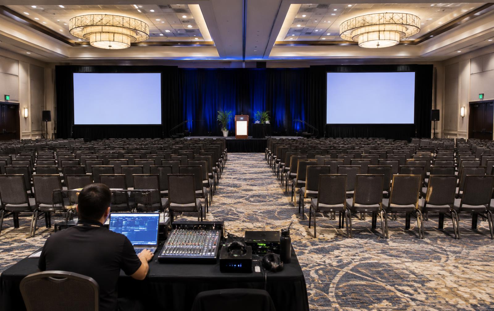 Hotel ballroom with dual projection screens and a technician at the AV table