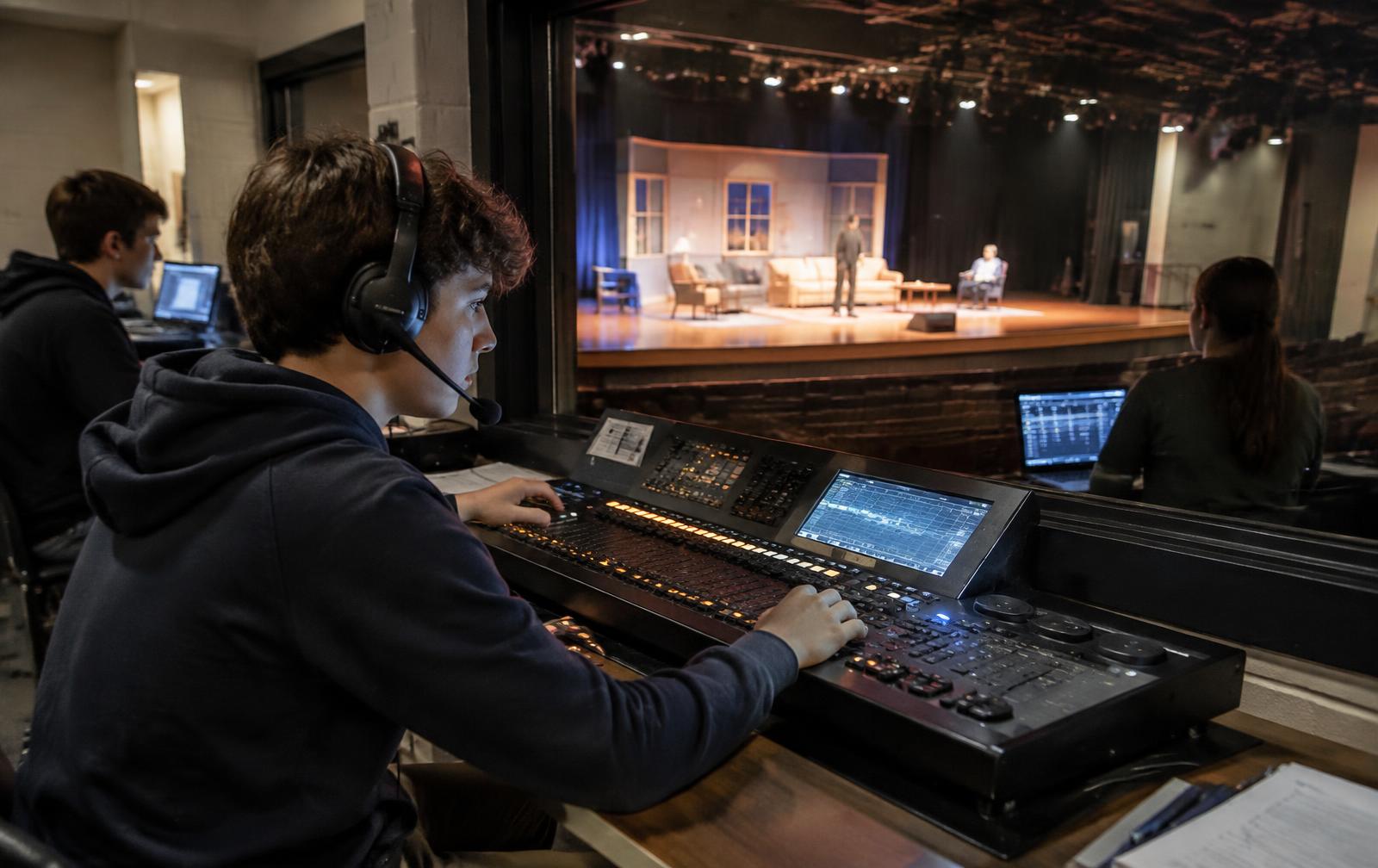 Student operating a lighting console in a school auditorium booth