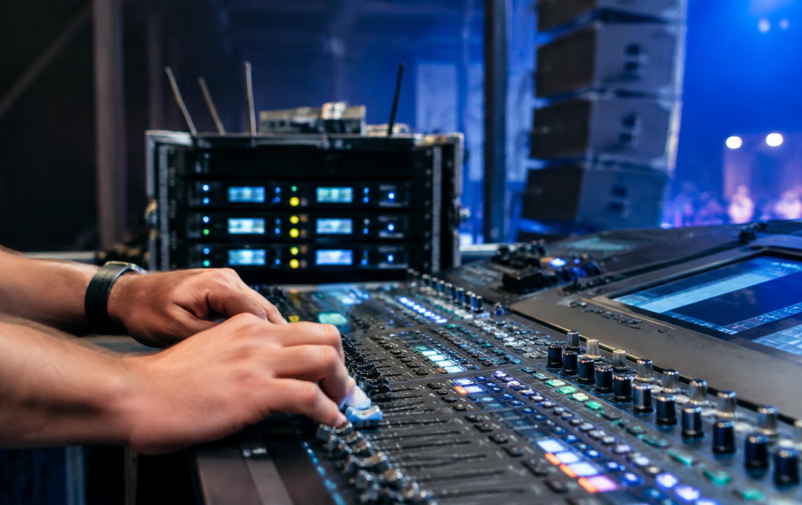 Audio engineer's hands on a digital mixing console with wireless microphone receivers behind