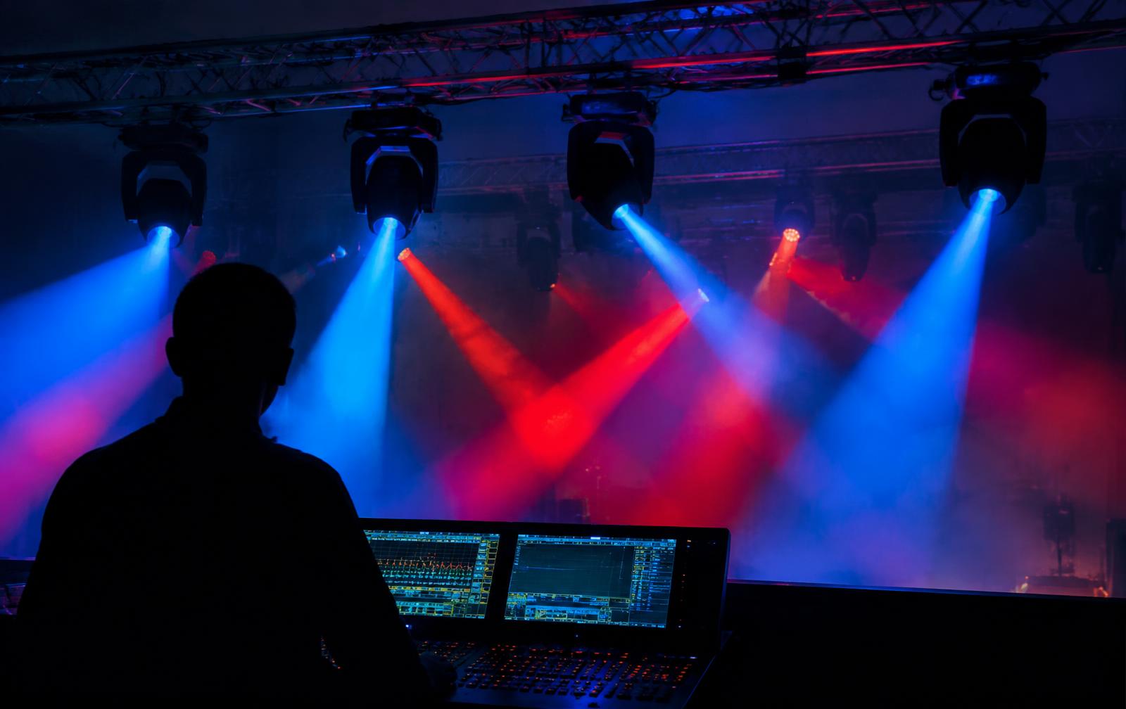 Lighting operator at a console in front of moving fixtures casting blue and red beams