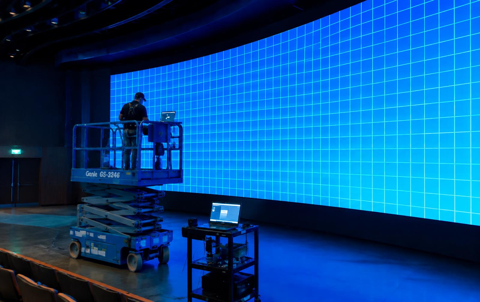 Technician on a lift calibrating a large curved LED video wall